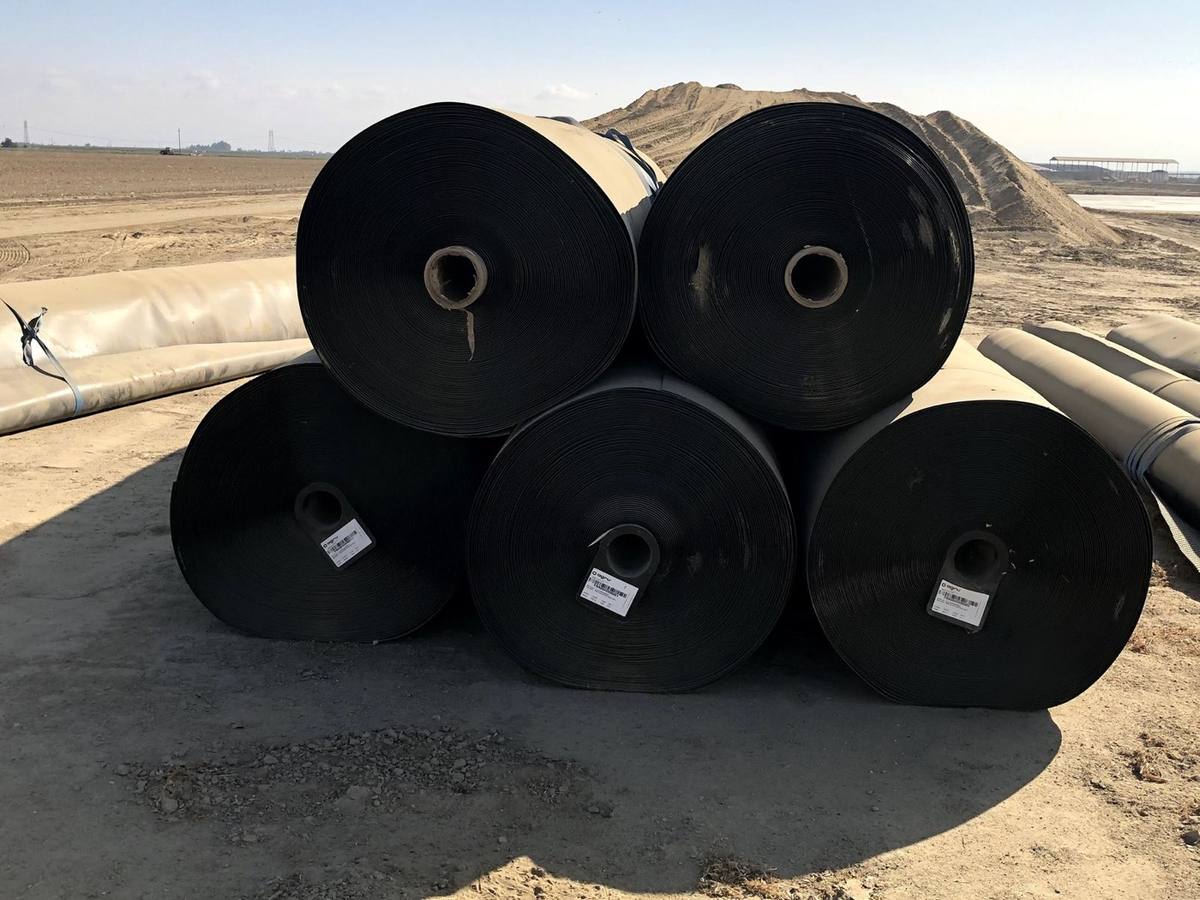 Five black geomembrane rolls stacked on a dirt pad