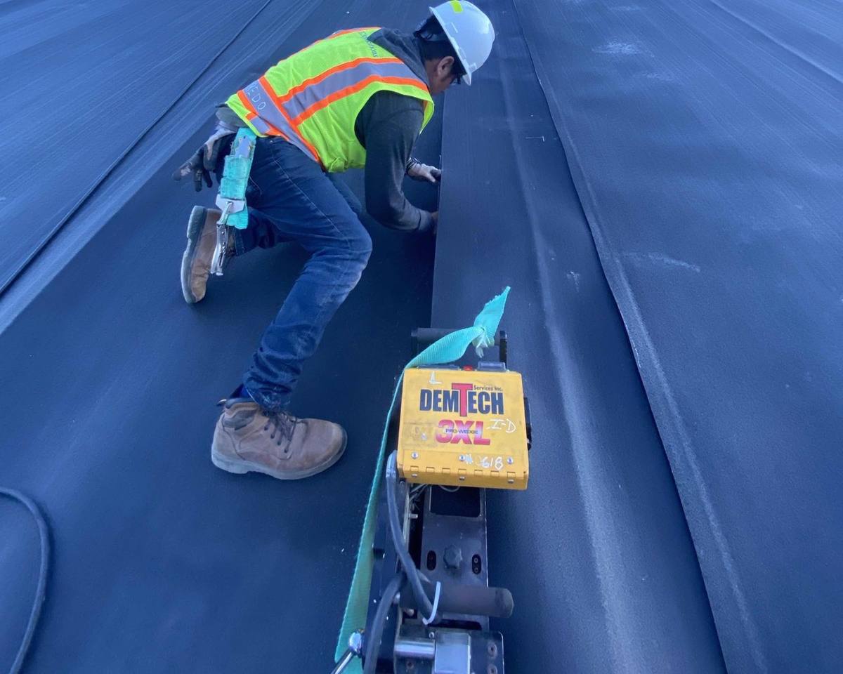 Installer working a geomembrane seam ahead of a DemTech Pro-Wedge 3XL welder